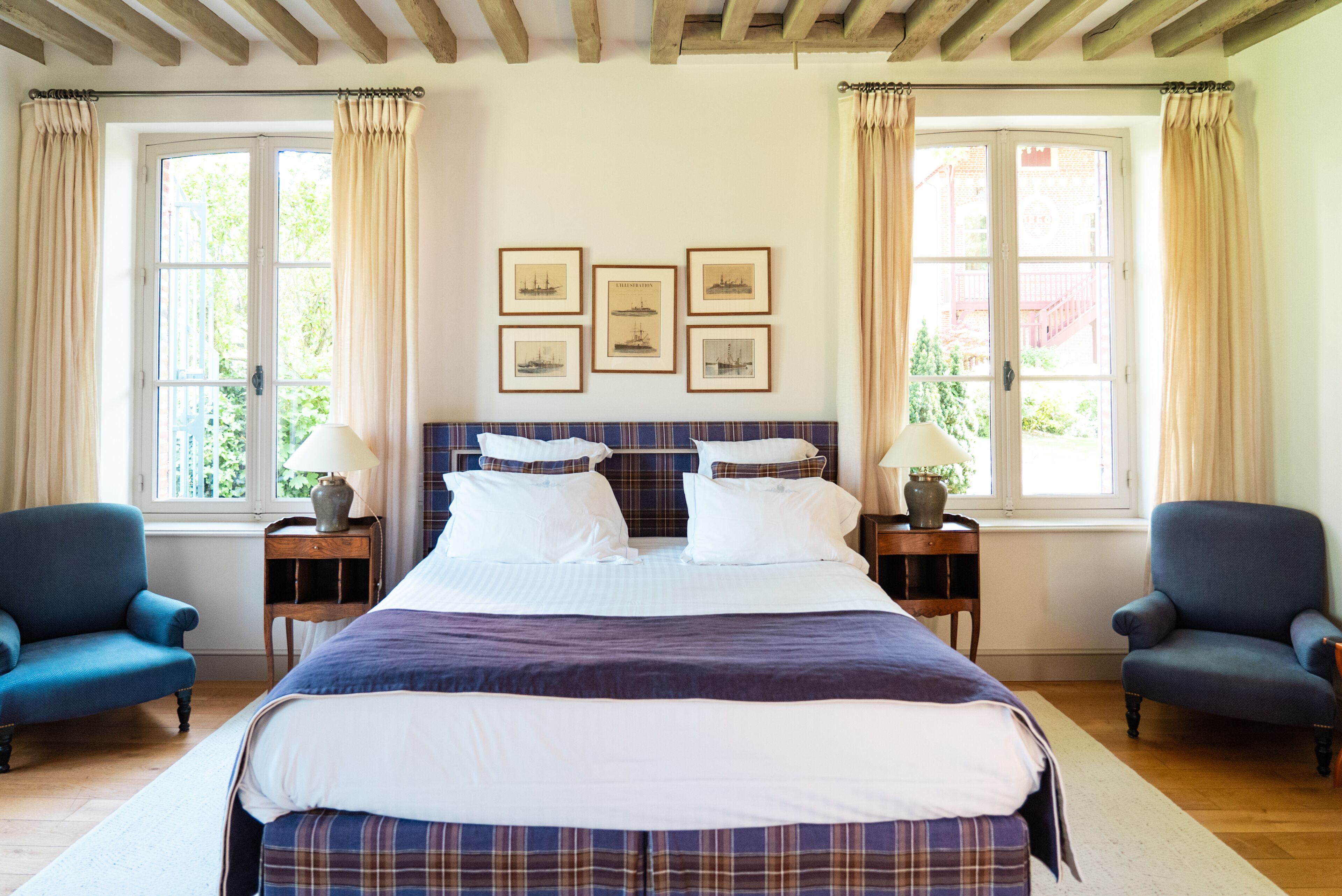 A bedroom with a large bed, two nightstands, two chairs, and a window with curtains.