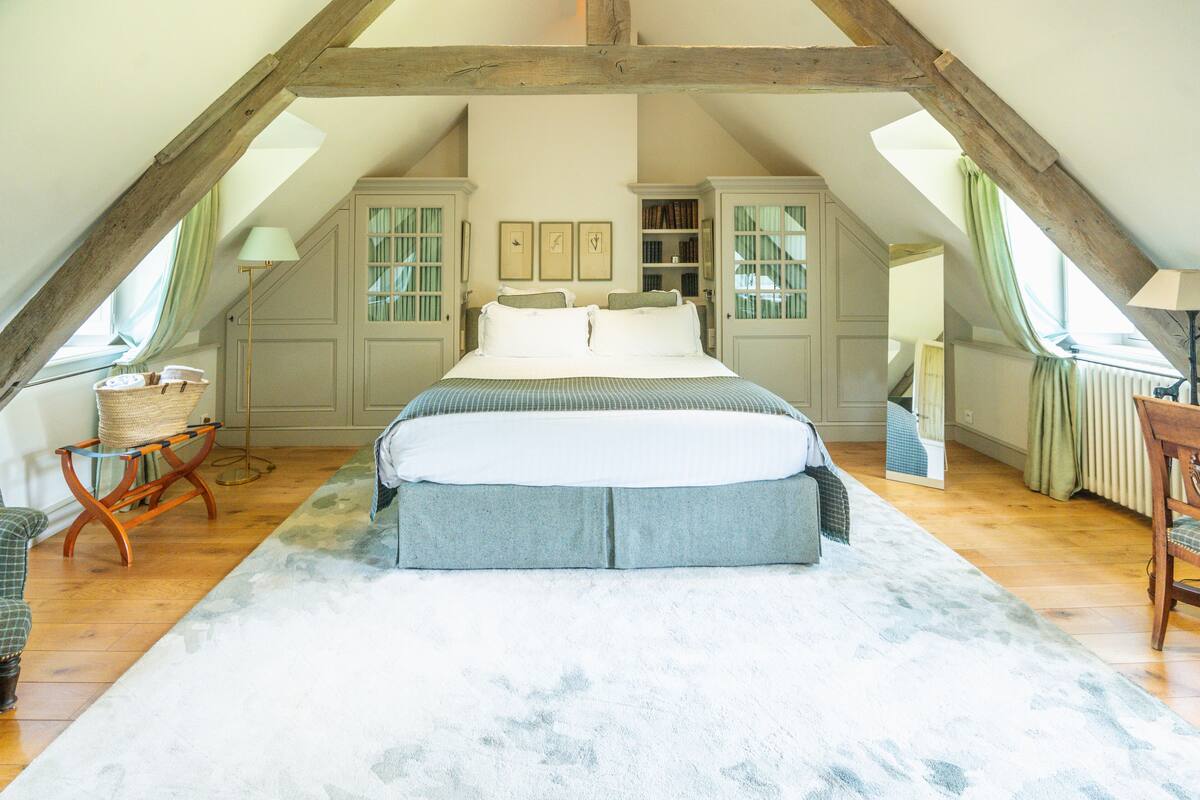 Quarto com uma cama grande, vigas de madeira, uma janela e uma cadeira.