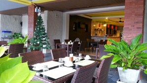An outdoor dining area with wicker tables and chairs, a Christmas tree, and potted plants. - Purimas Resortel (Rawai)