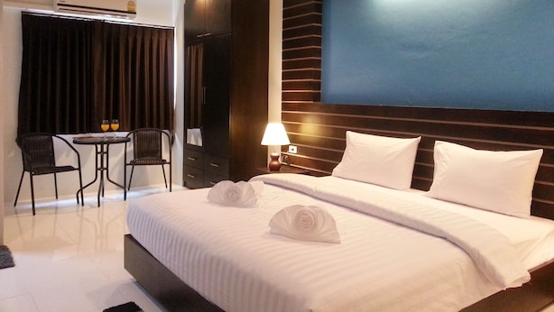 A hotel room with a large bed, a desk with two chairs, a lamp, and a view of the city. - Purimas Resortel (Rawai)