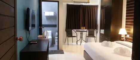 A hotel room with a bed, a desk, a chair, a small table with two glasses of orange juice, and a TV on the wall.