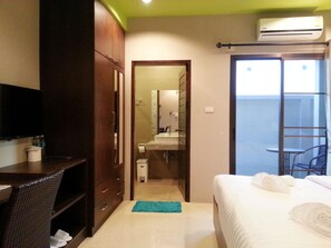 A hotel room with a bed, a desk, a wardrobe, a bathroom with a mirror, and a balcony with a chair. - Purimas Resortel (Rawai)