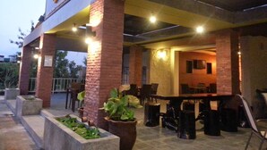 An outdoor seating area with brick pillars, potted plants, and a bar with chairs. - Purimas Resortel (Rawai)