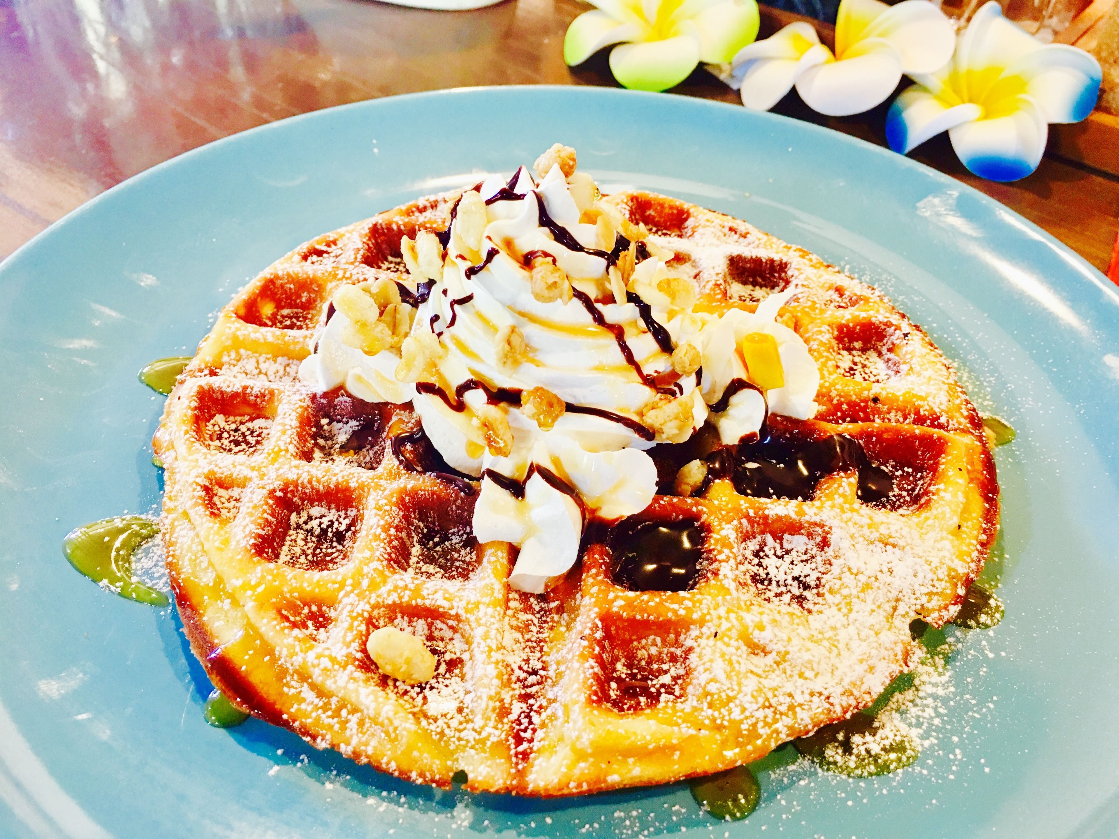 A waffle with whipped cream and chocolate syrup on a blue plate.