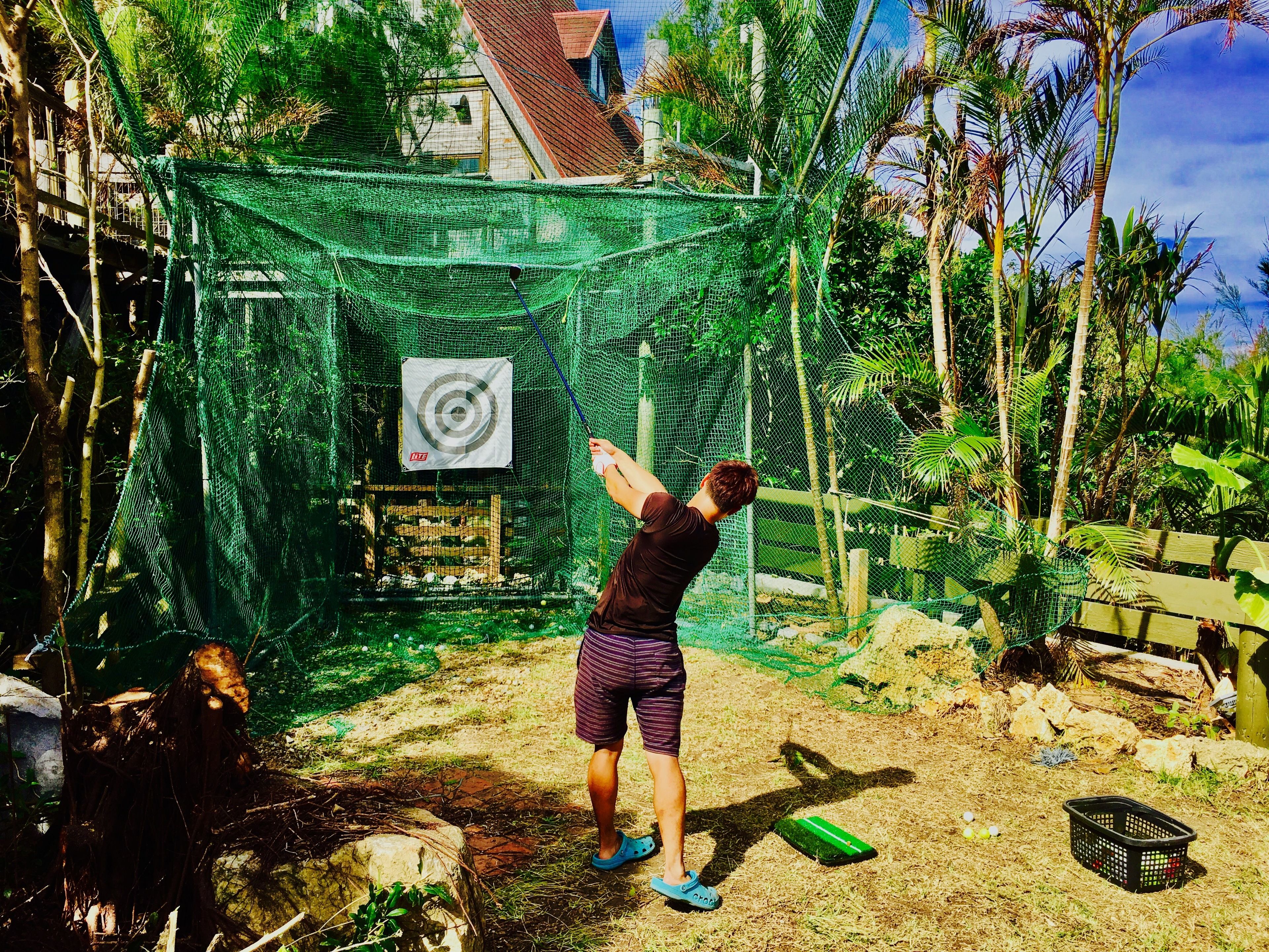 Una persona practica swings de golf en un área con red y un tablero de objetivo.