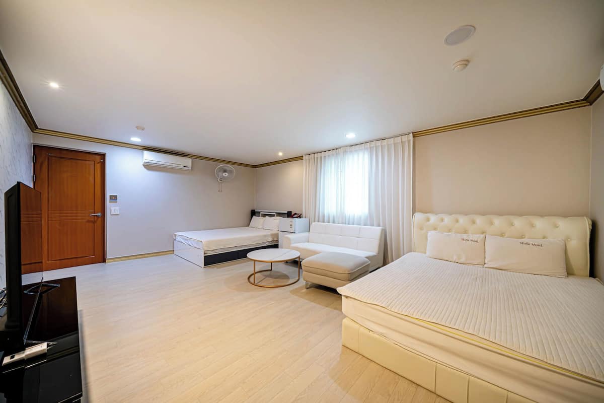 A spacious hotel room with a large bed, a sofa, a small round table, and a TV.