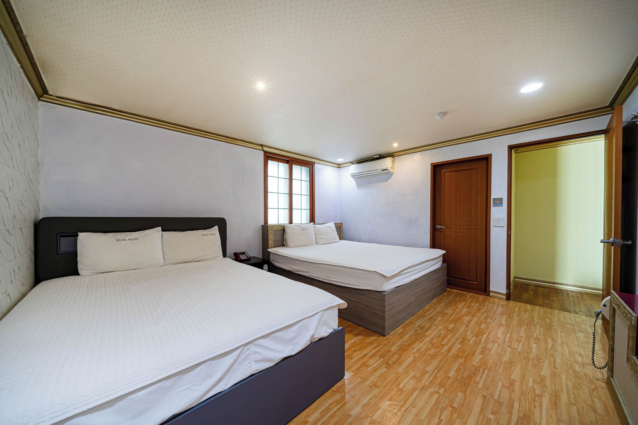 A bedroom with two beds, a wooden floor, a window, and an air conditioning unit.