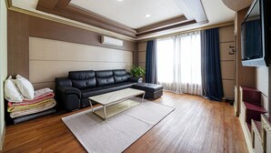 A modern living room with a black leather sofa, a glass coffee table, and a wooden floor. - Sense Motel (Busan)