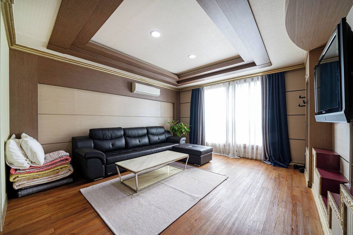 A modern living room with a black leather sofa, a glass coffee table, and a wooden floor.