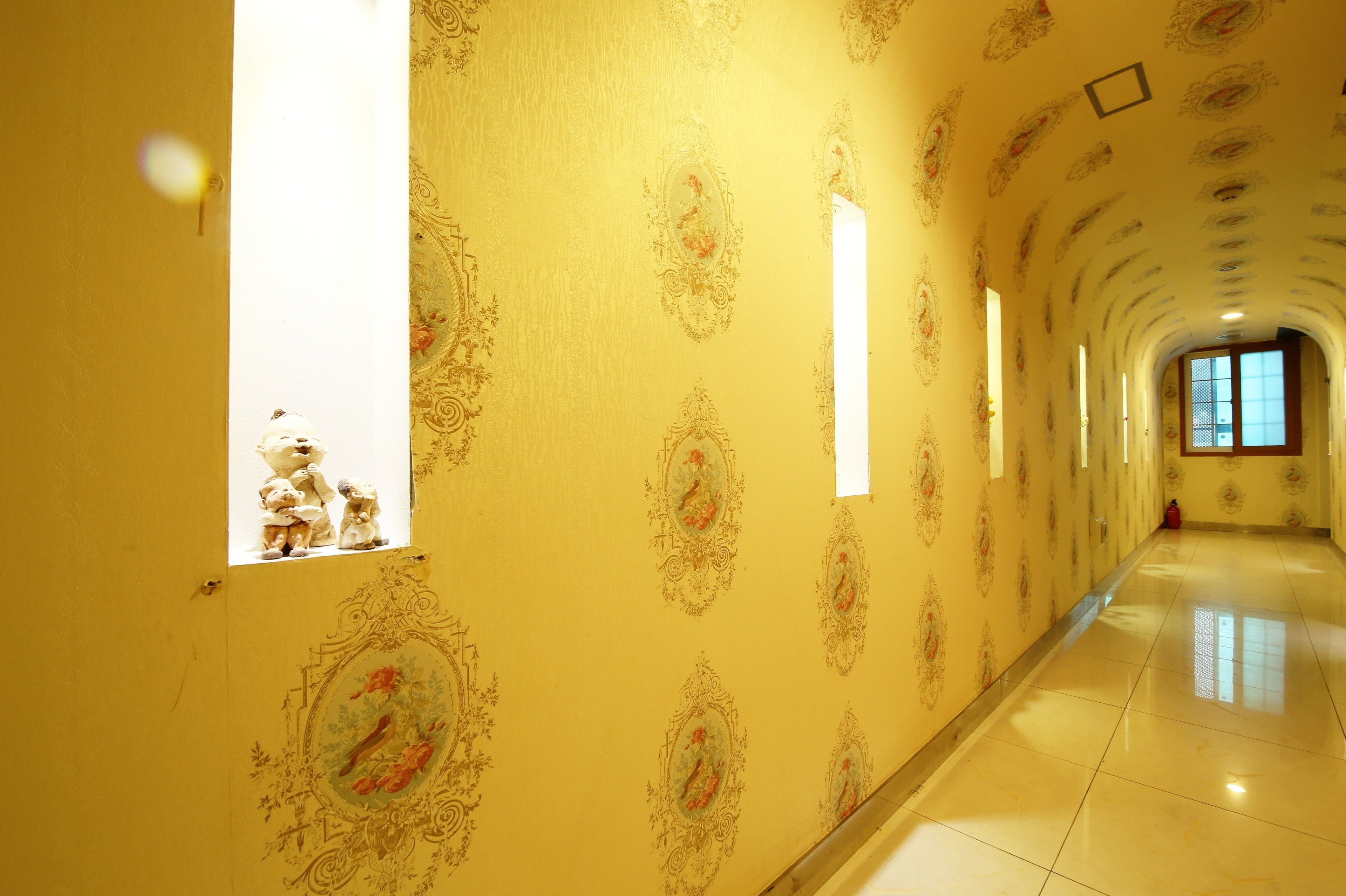 A hallway with ornate wallpaper, a row of framed pictures, and a tiled floor.