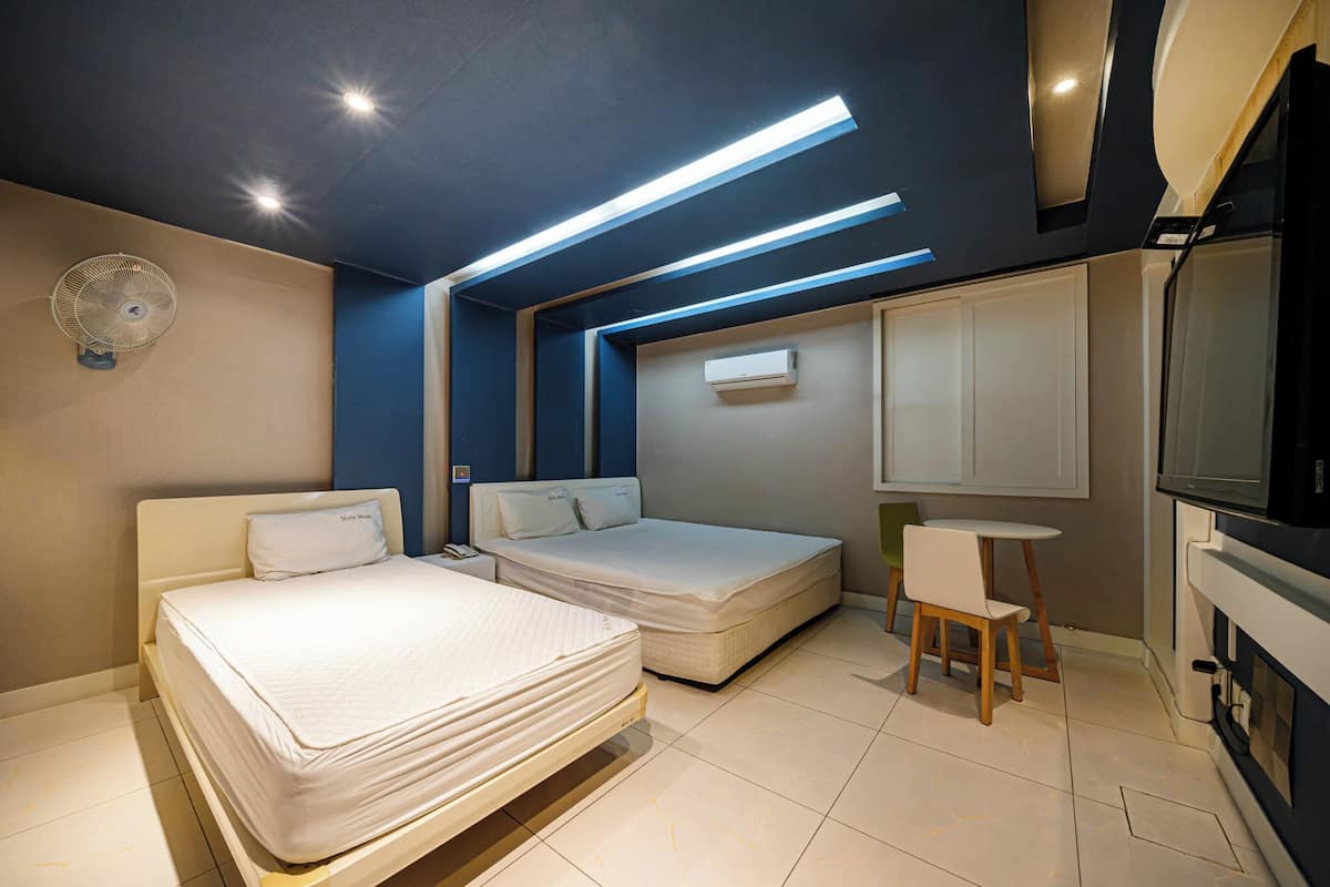 A modern bedroom with two beds, a small table, and a TV.