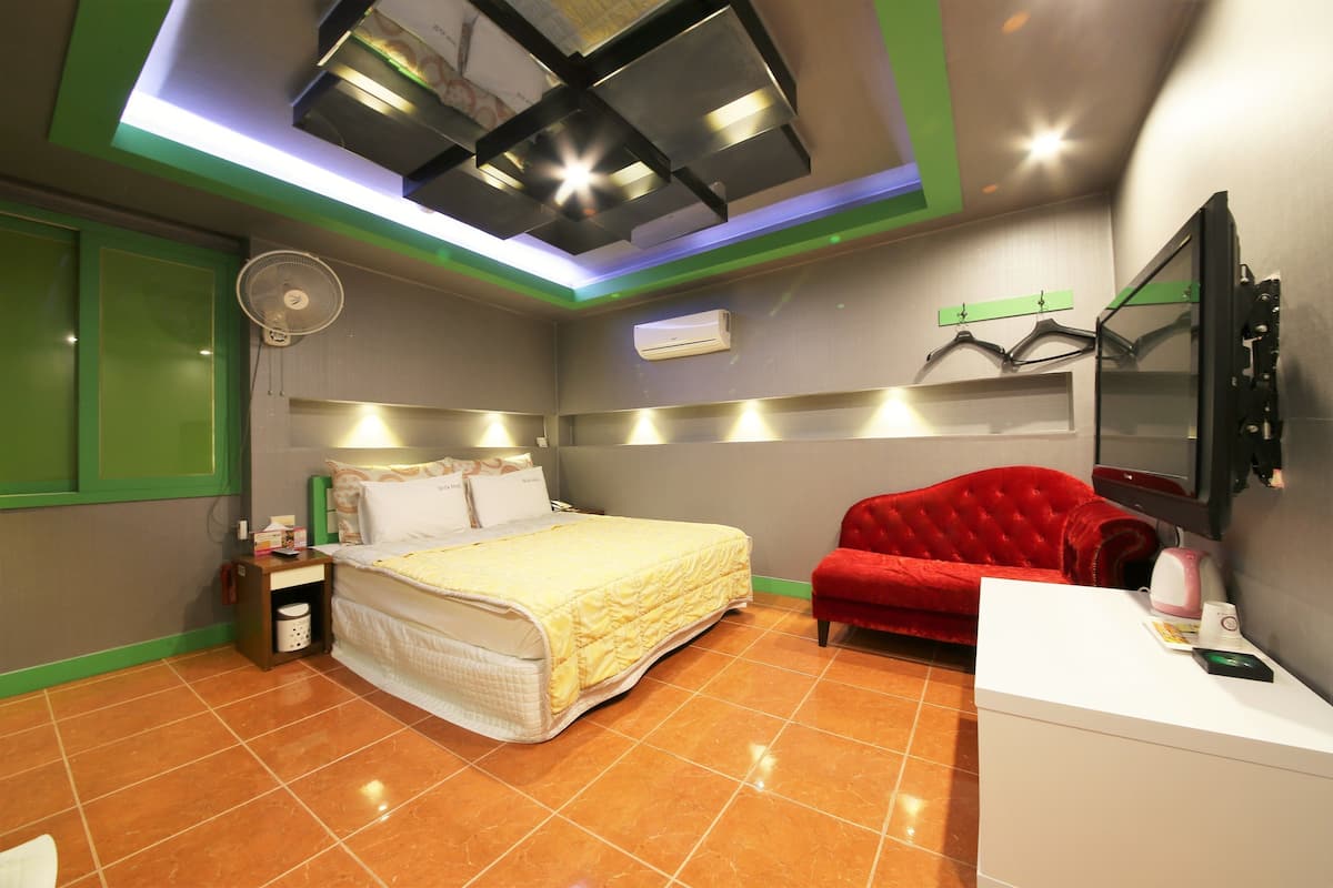 A hotel room with a bed, a red sofa, a white desk, and a ceiling fan.