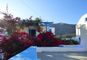 A white building with blue accents, a balcony, and pink flowers in front.