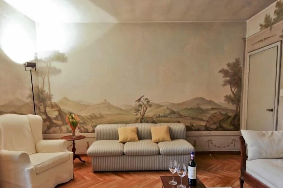 A living room with a sofa, armchairs, and a painting of a landscape on the wall.