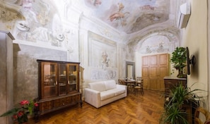 A room with a herringbone wooden floor, a white sofa, a wooden cabinet with glass doors, and a ceiling with frescoes. - Florentapartments - Ponte Vecchio (Florence)