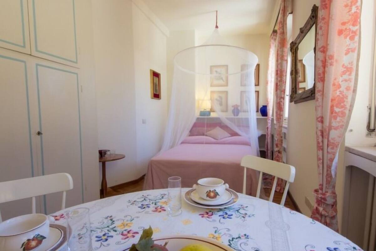 A bedroom with a bed under a canopy, a bedside table with a lamp, and a chair.