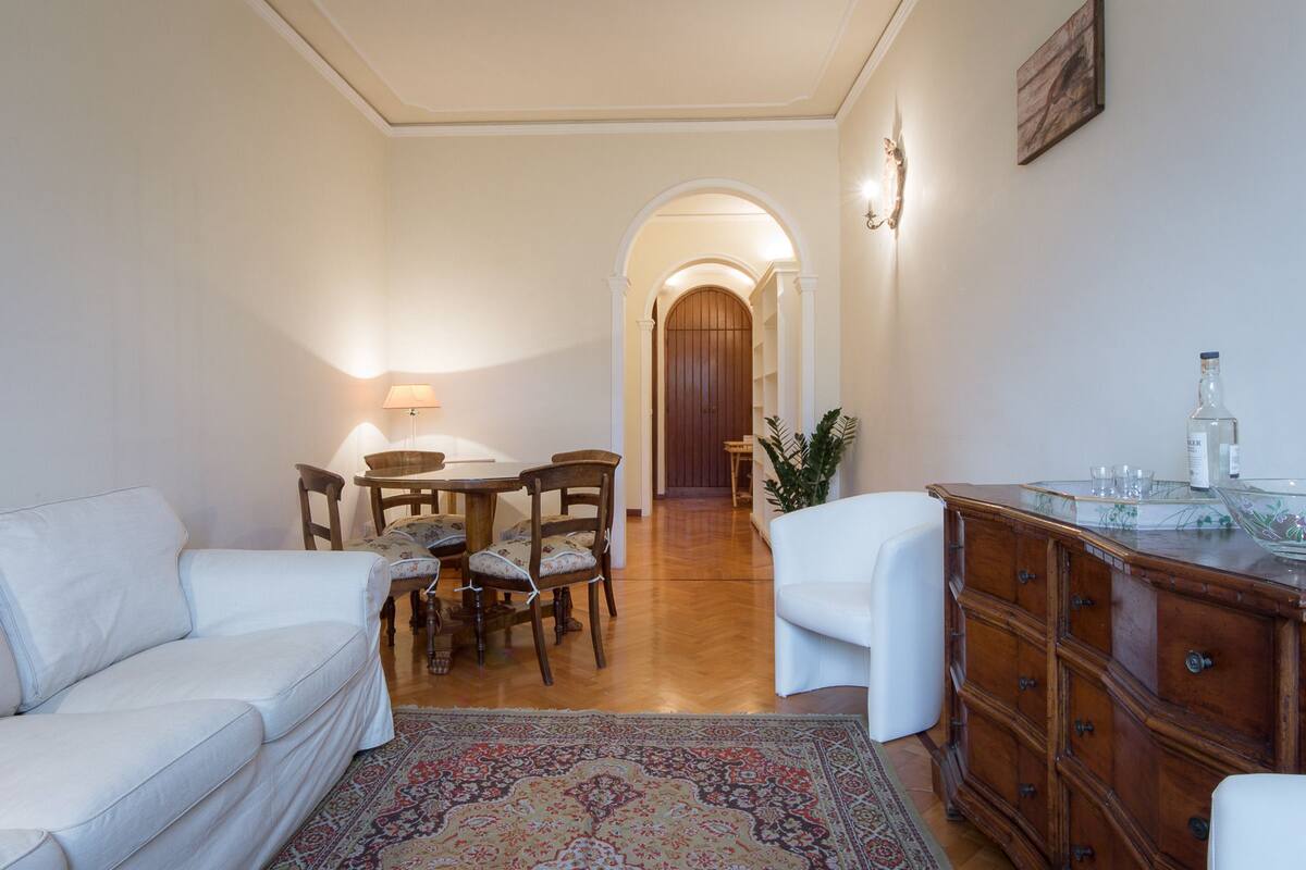 A living room with a sofa, a dining table with chairs, a cabinet, and a rug.