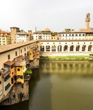 A riverside view of a historic city with buildings along the water, including a bridge and a tower. - Florentapartments - Ponte Vecchio (Florence)