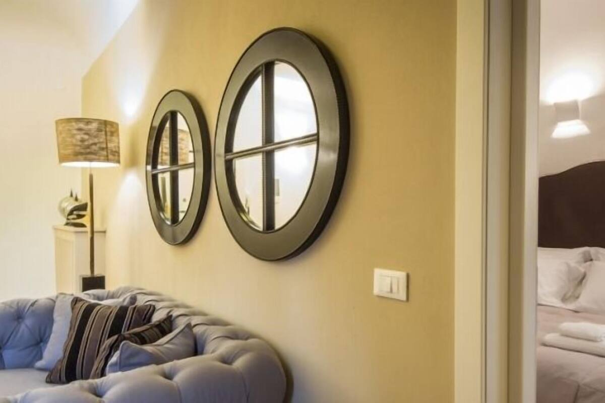 A hotel room with a bed, a sofa, and two wall-mounted mirrors.