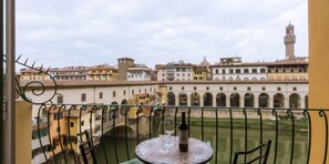 A balcony with a table and chairs, overlooking a historic building with arches and a tower. - Florentapartments - Ponte Vecchio (Florence)