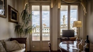 A room with a large window, a television, a dining table with wine glasses, and a potted plant. - Florentapartments - Ponte Vecchio (Florence)