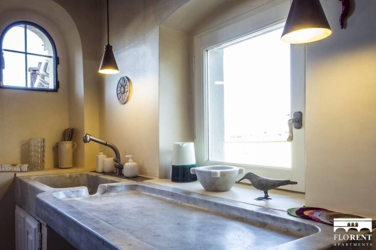 A kitchen with a marble countertop, a window, and pendant lighting.