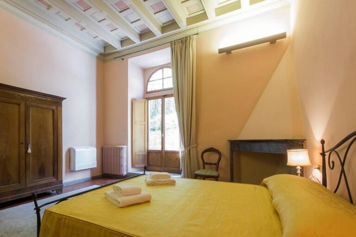 A bedroom with a bed, a wooden wardrobe, a radiator, a chair, and a fireplace.