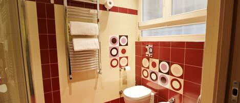A bathroom with a glass shower enclosure, a towel rack with white towels, a toilet, and a sink.