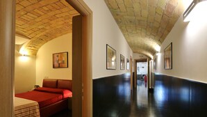 A hotel corridor with a tiled floor, a bed with a red bedspread, and framed artwork on the walls. - Residenza Adriana (Rome)