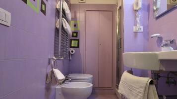 A bathroom with a toilet, sink, and shower. There are towels hanging on the wall and a mirror above the sink.