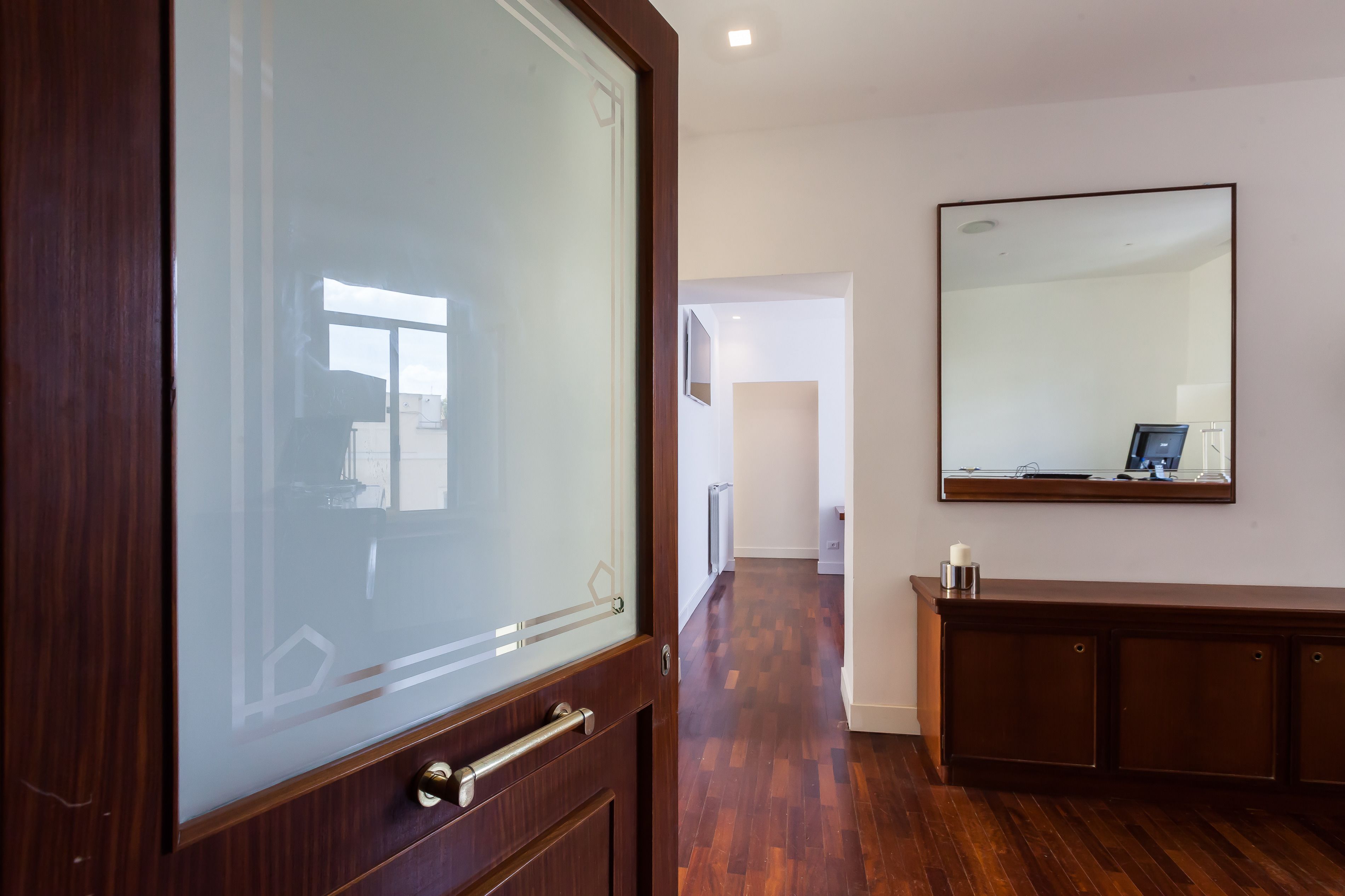 Un pasillo con suelo de madera, puerta de cristal y un espejo grande en la pared.