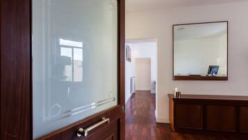 Un pasillo con suelo de madera, puerta de cristal y un espejo grande en la pared.