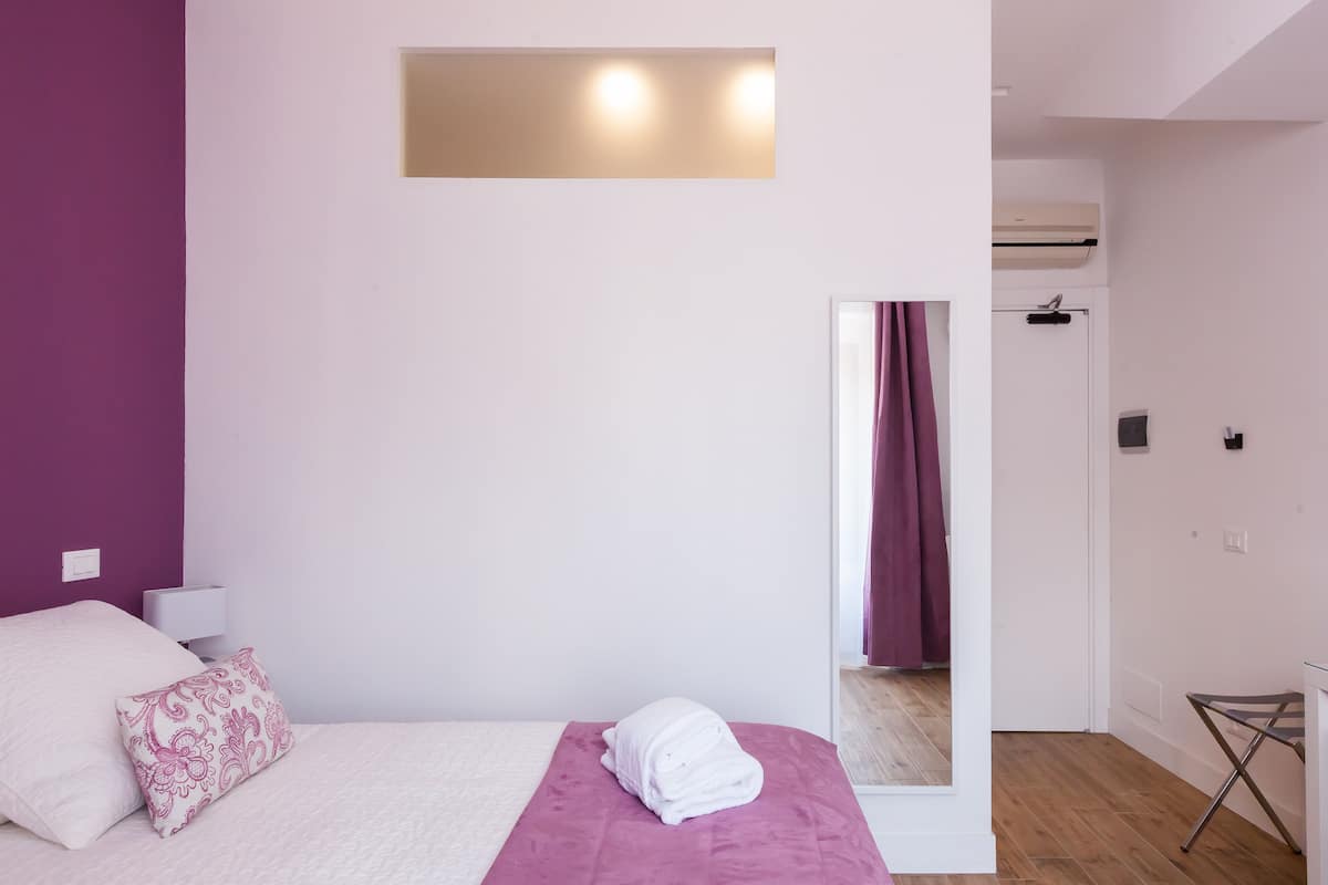 Une chambre à coucher comprenant un lit, une table de chevet, un miroir et une porte donnant sur une salle de bain.