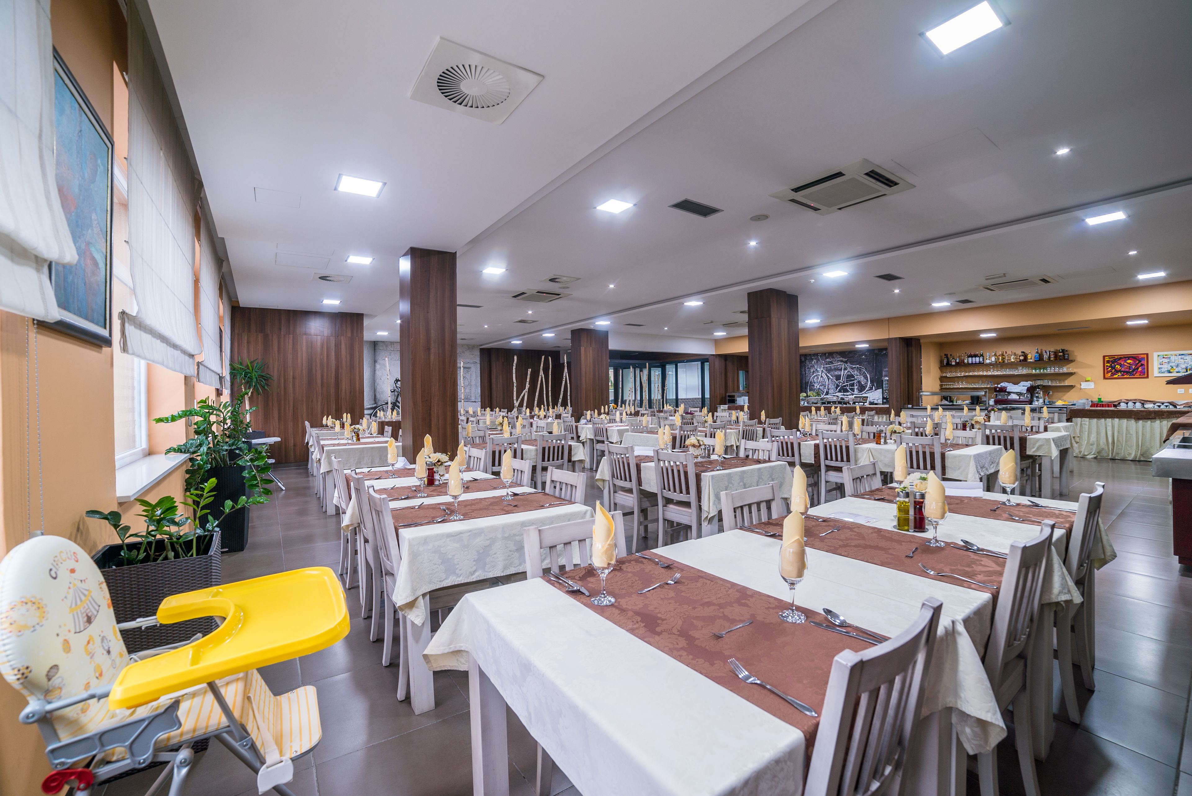 A large dining hall with multiple tables set for service, a children's play area, and a bar area.