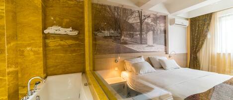 Une chambre d’hôtel avec une grande baignoire, un lit avec du linge de maison blanc et une fresque représentant un paysage de parc sur le mur.