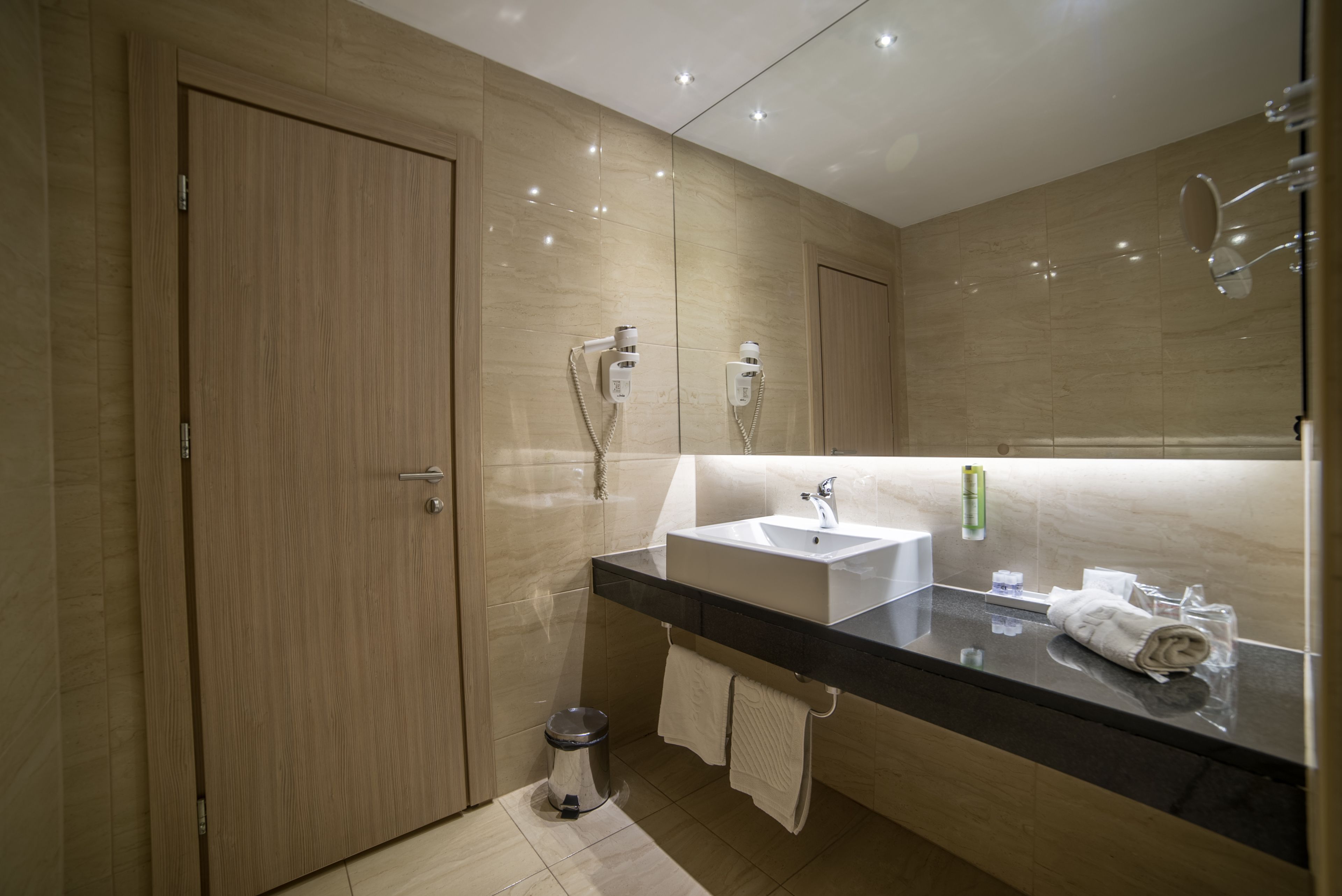 A modern bathroom with a wooden door, a black countertop sink, a mirror, and a towel on the counter.