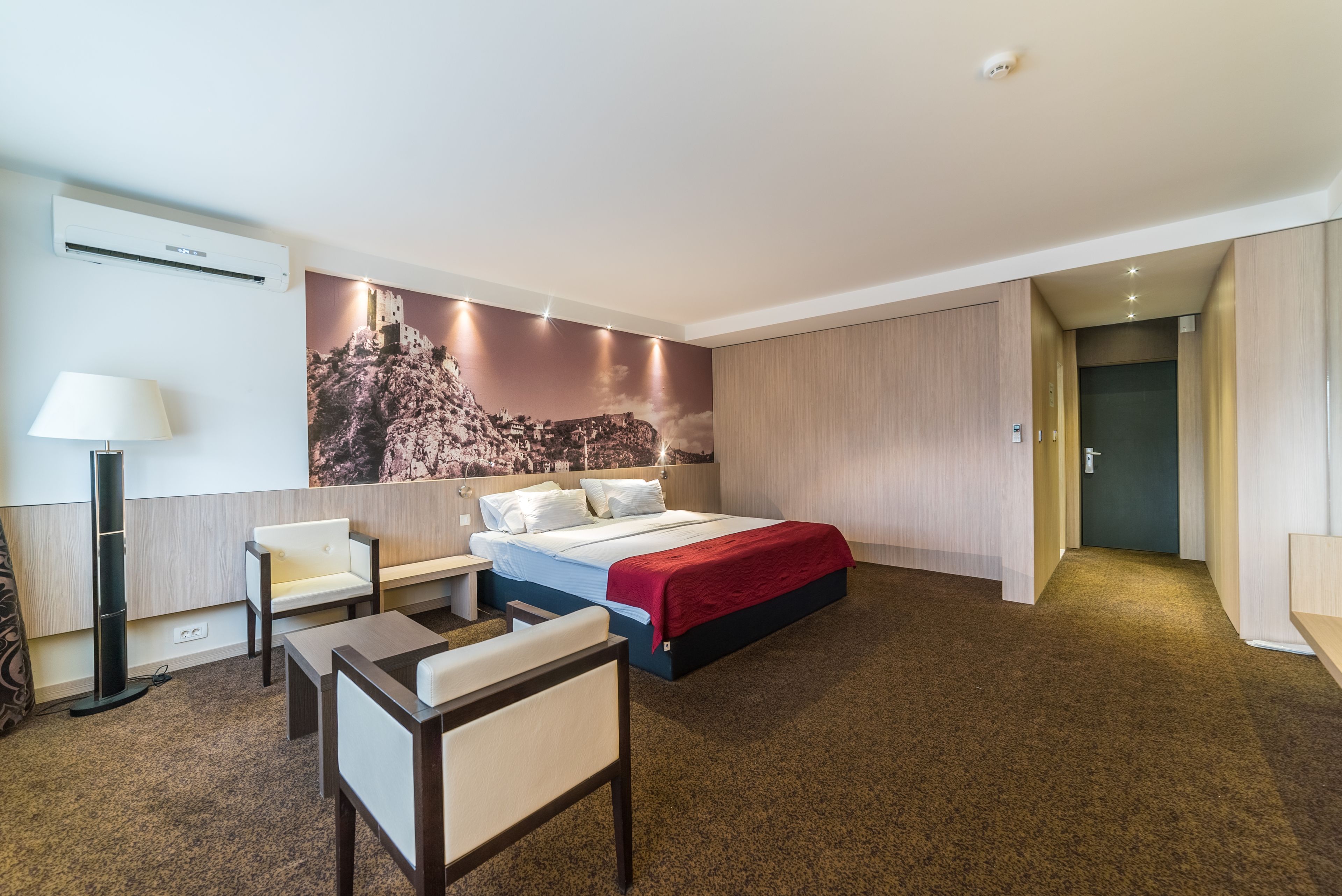 A hotel room with a bed, a desk, a chair, a lamp, and a large wall mural.