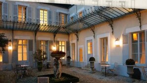 Een binnenplaats met een fontein, terrasmeubels en een overdekt gedeelte met een pergola.