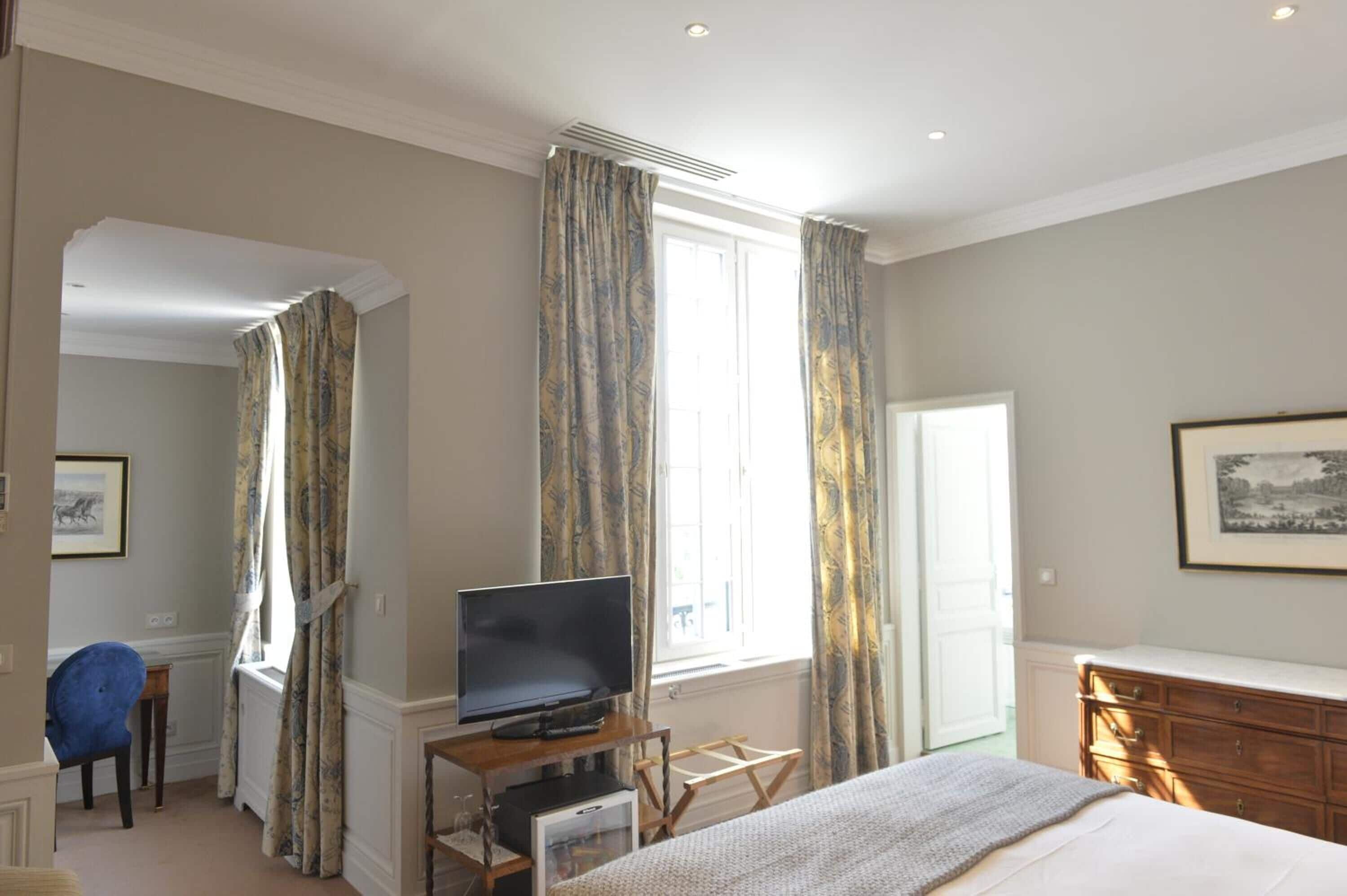 Habitación de hotel con cama, televisor sobre un mueble de madera, cómoda y una silla.