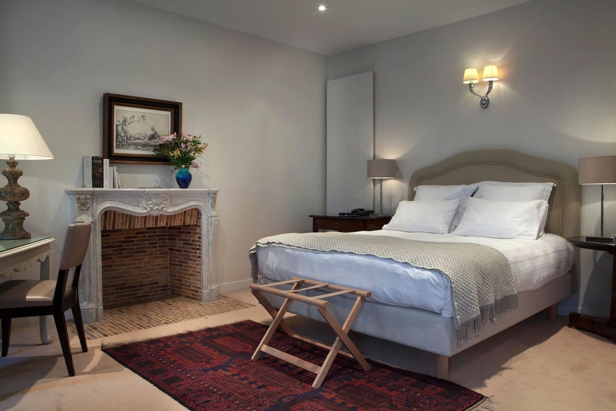 Een slaapkamer met een bed, nachtkastjes, een open haard, een stoel en een vloerkleed.