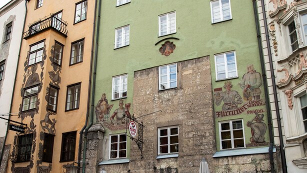 Una hilera de mesas de café al aire libre con sombrillas, frente a edificios históricos y coloridos.