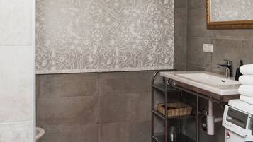 A bathroom with a patterned shower curtain, a red rug, a washing machine, and a sink with a towel rack.