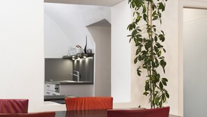 Un comedor moderno con una mesa y sillas, una cocina al fondo y una planta en maceta.