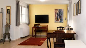 A room with a dining table, chairs, a TV, a radiator, and a painting on the wall.
