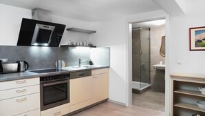 Una cocina moderna con horno empotrado, lavavajillas y microondas. Se ve una ducha a través de una puerta abierta.