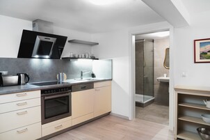 Eine moderne Küche mit Einbauofen, Geschirrspüler und Mikrowelle. Durch eine offene Tür ist eine Dusche sichtbar.