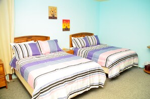 A bedroom with two beds, each with striped bedding, wooden headboards, and bedside tables. - Wildgreen Residence (Point Fortin)