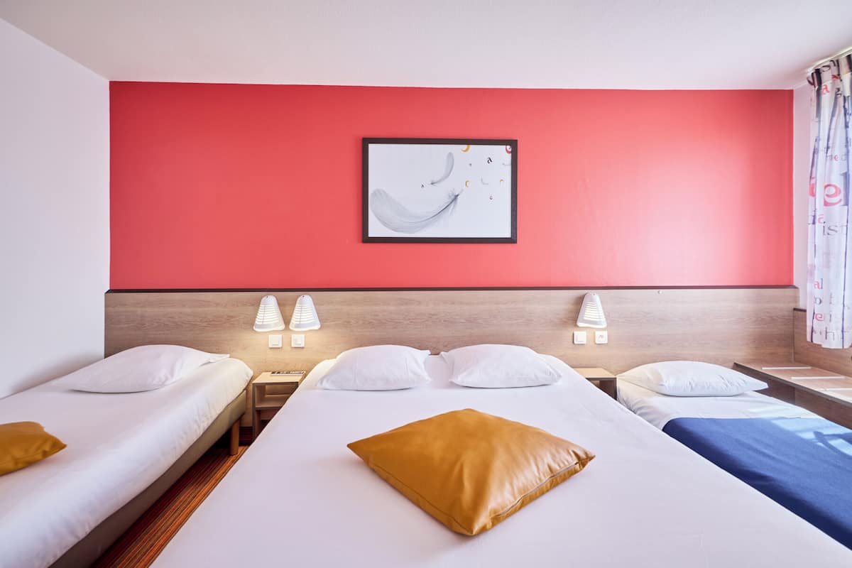 A hotel room with two beds, a red accent wall, and a framed artwork above the beds.