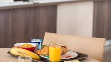 A breakfast tray with croissants, a banana, a glass of orange juice, a croissant, a cup, and a small container of yogurt on a table in a modern kitchen setting.