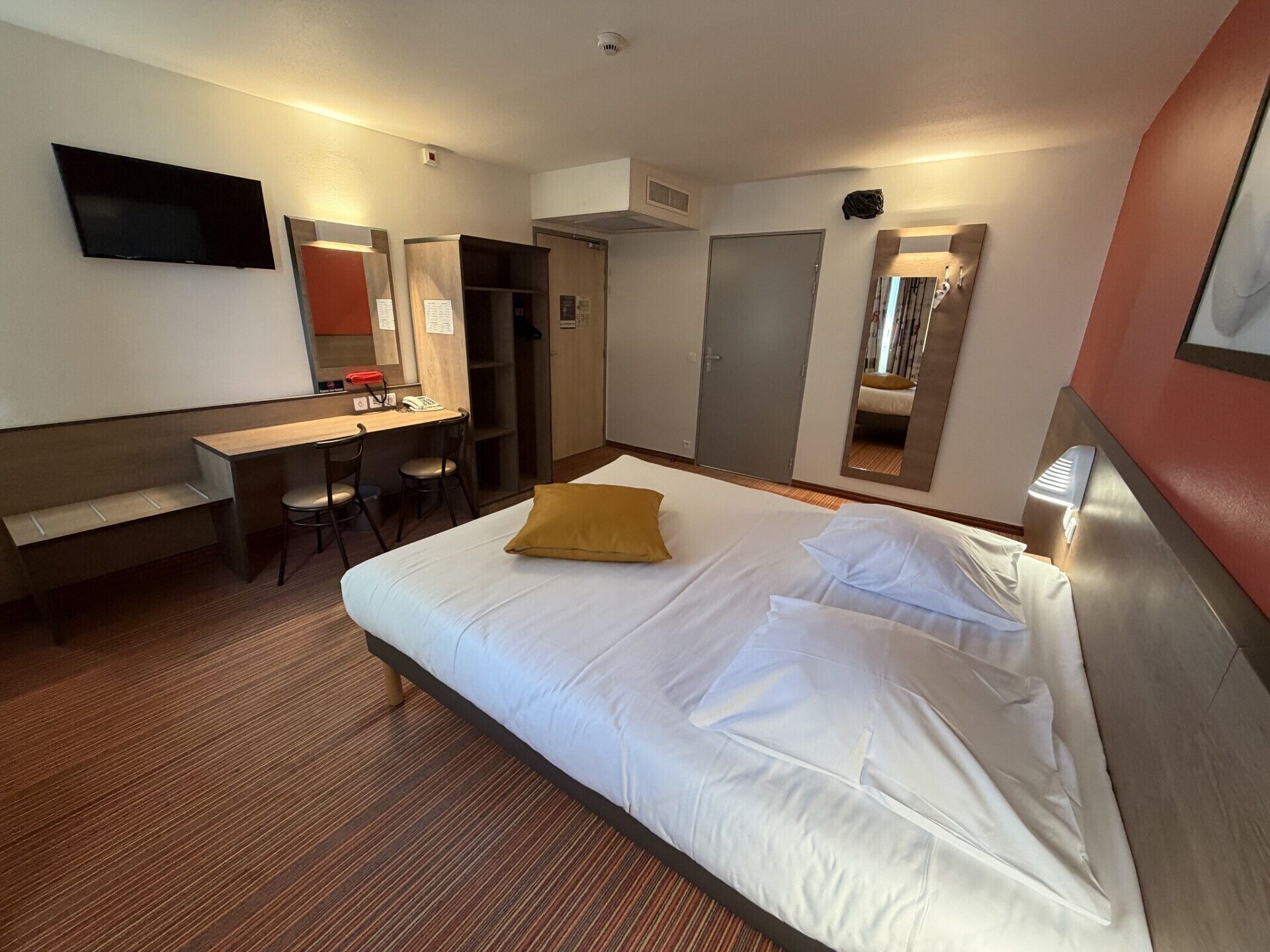 Habitación de hotel con cama, escritorio, silla, armario y televisor.